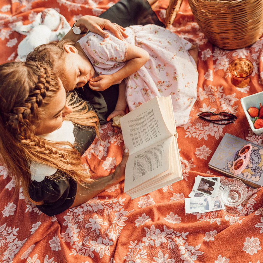Photo of a mother reading to her daughter while on a picnic